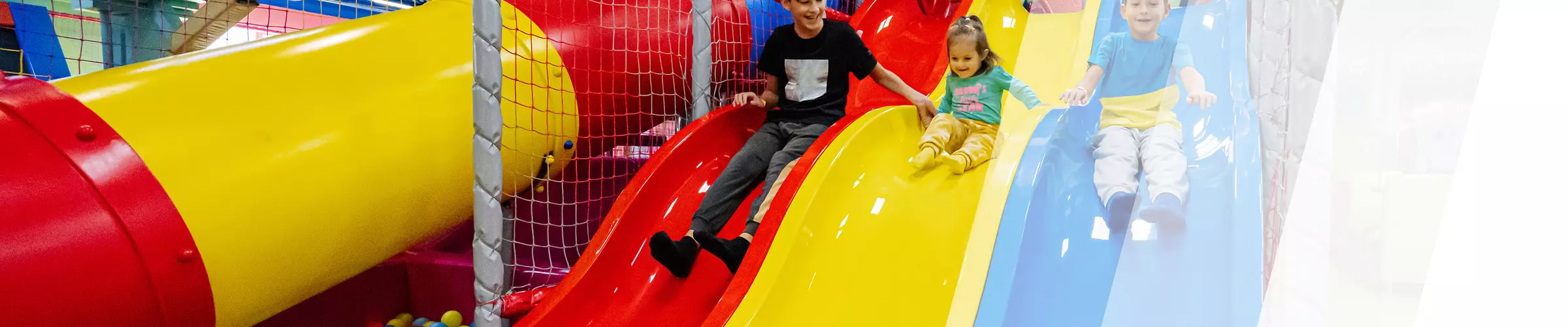 Kinder rutschen auf einer Indoor-Wellenrutsche ins Bällebad