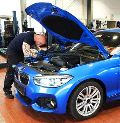 Ein Kfz-Sachverständiger blickt in einer Werkstatt in den Motorraum eines Fahrzeugs mit geöffneter Motorhaube
