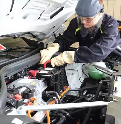 Ein Sachverständiger mit Schutzkleidung prüft die Technik eines Elektroautos