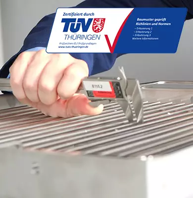 Hand mit Schieblehre misst Abstände eines Grillrostes darüber ein TÜV Thüringen Prüfzeichen