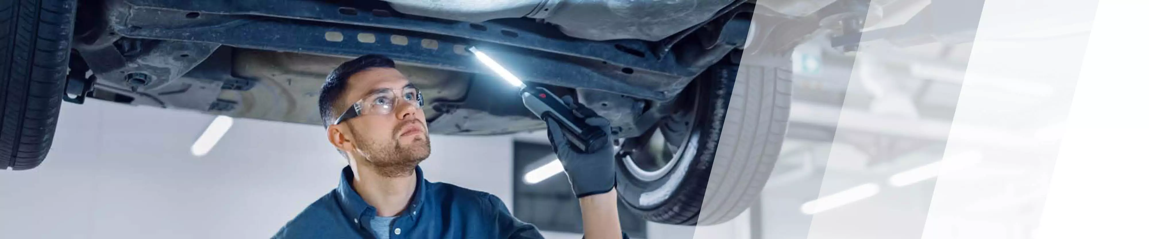 Ein Prüfer schaut mit einer Lampe unter ein Auto