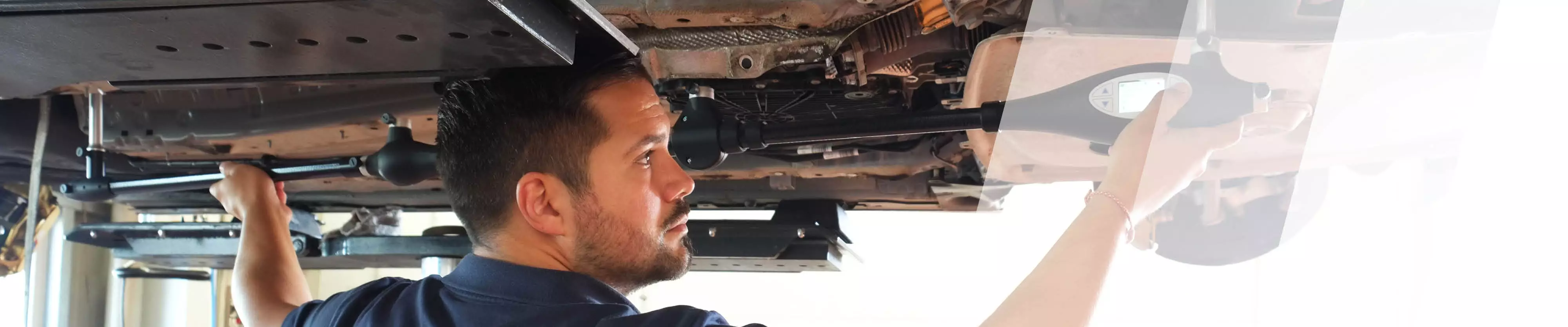 Ein Prüfer begutachtet mit einem Messgerät den Schaden unter einem Auto