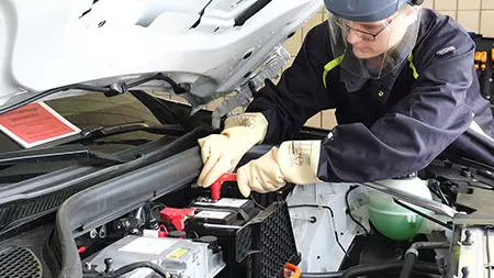 Kfz-Mechatroniker mit Schutzausrüstung an einem Elektroauto